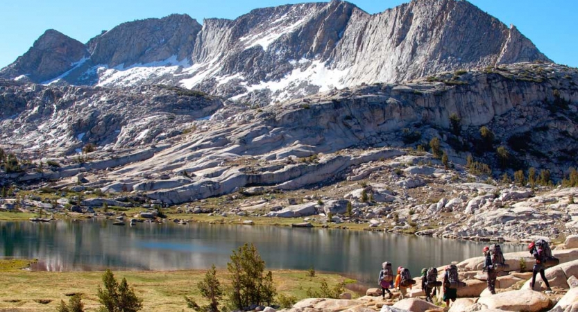 A group of people hike near an alpine lake, with a large mountain in the background. 